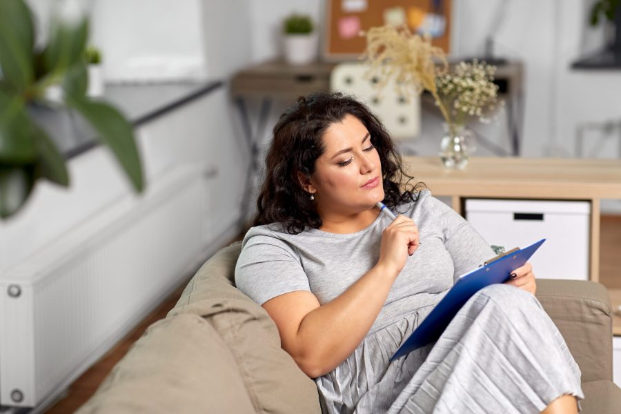 young contemplative woman sitting on her couch looking at a notepad